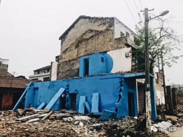 △ 這棟建筑是臨江最近的半拆遷建筑物的遺留，沅江和堤壩成為了展覽的天然背景。創(chuàng)作團隊對這棟建筑進行了半涂裝，將符號性的沅水曲線與拆遷進行中的建筑立面進行意義的疊造，它們共同觸發(fā)了場所空間多元語境的生成，把拆遷這種暫時破壞性、干擾性的介入行動與沅水右岸發(fā)展的未來性、美好性緊密融合。